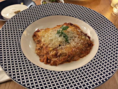 Picture of lasagne main course on a nice branded colours plate of white line and blue sqaures.